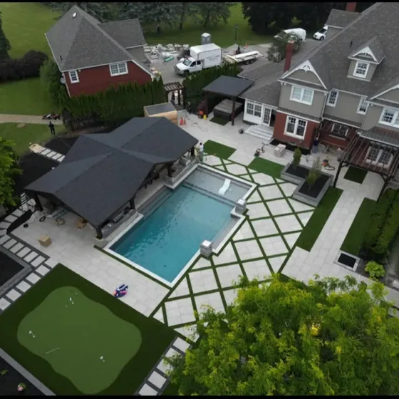Drone view of a finished backyard with pool, cabana, putting green and interlock patio