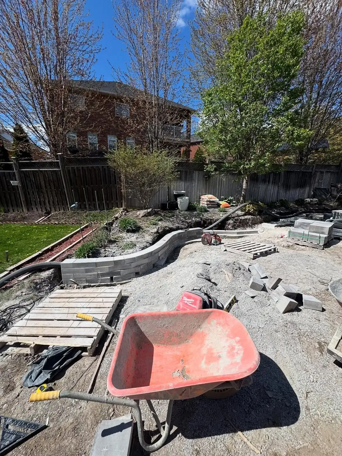 An MWG build underway: retaining wall course going in, pallets and granular base across the yard